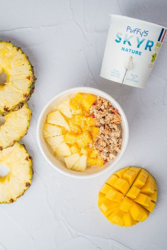 Un bowl gourmand composé de skyr nature sans matière grasse, avec des dés de fruits frais ( ananas et mangue) et du granola. Le